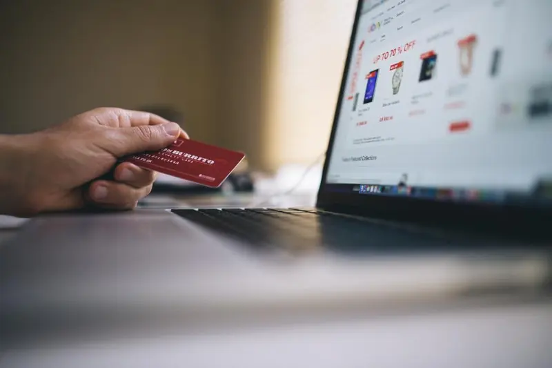 Mano con una tarjeta de crédito frente a una laptop con una tienda online abierta