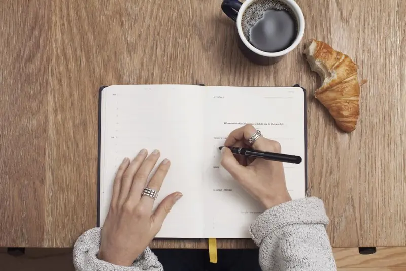Manos escribiendo en un cuaderno junto a un café