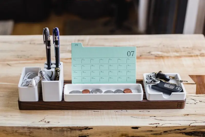 Calendario de escritorio junto a plumas y un organizador sobre una mesa de madera