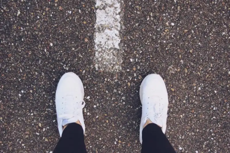Pies con tenis blancas parados frente a una línea pintada en el asfalto